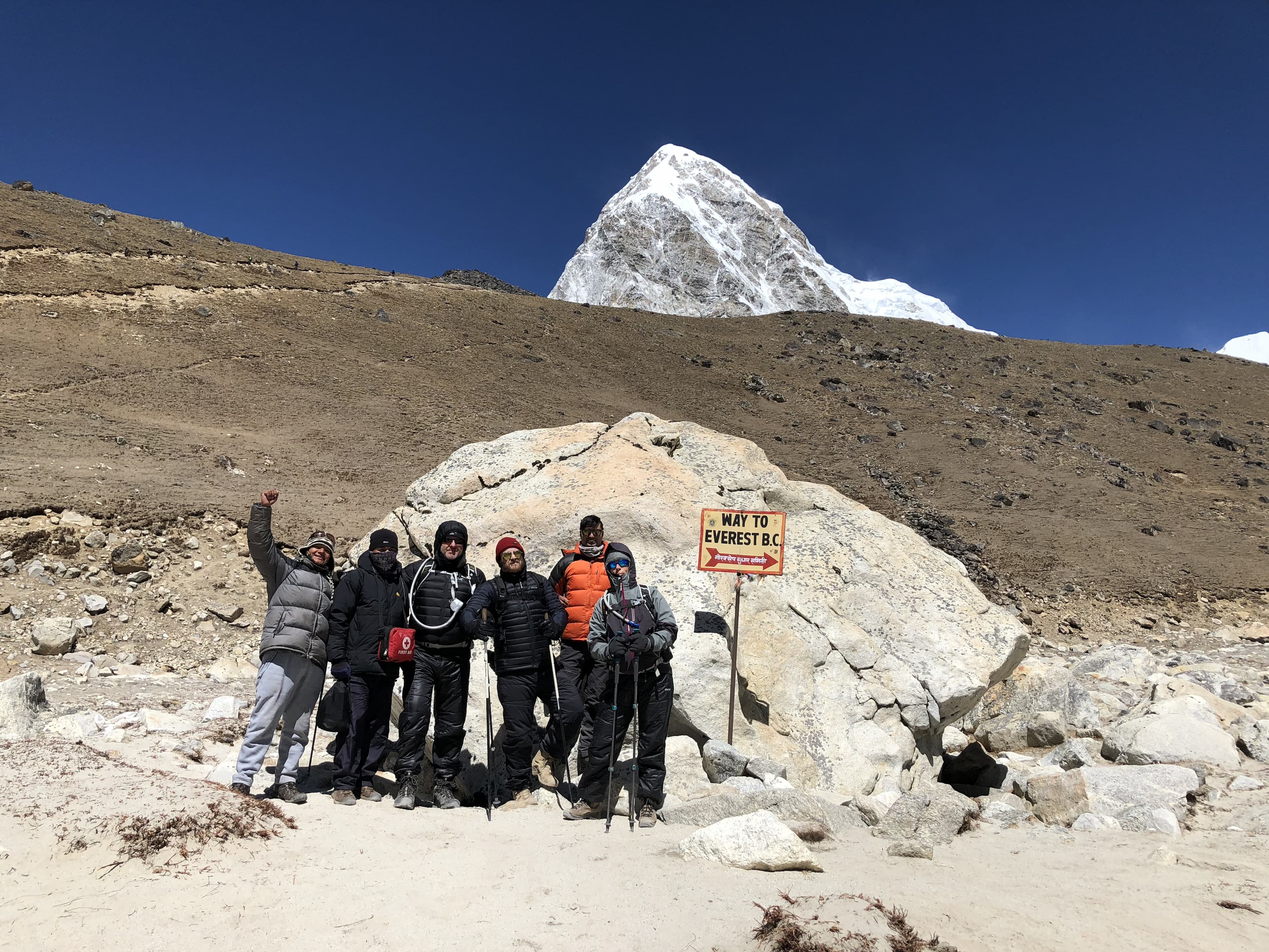 Climbers at the Everest Base Camp sign with snow-capped peak behind