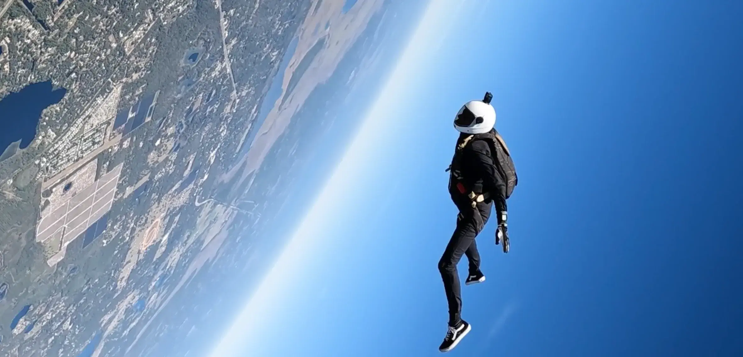 A skydiver in freefall high above the coast, the earth curving away below